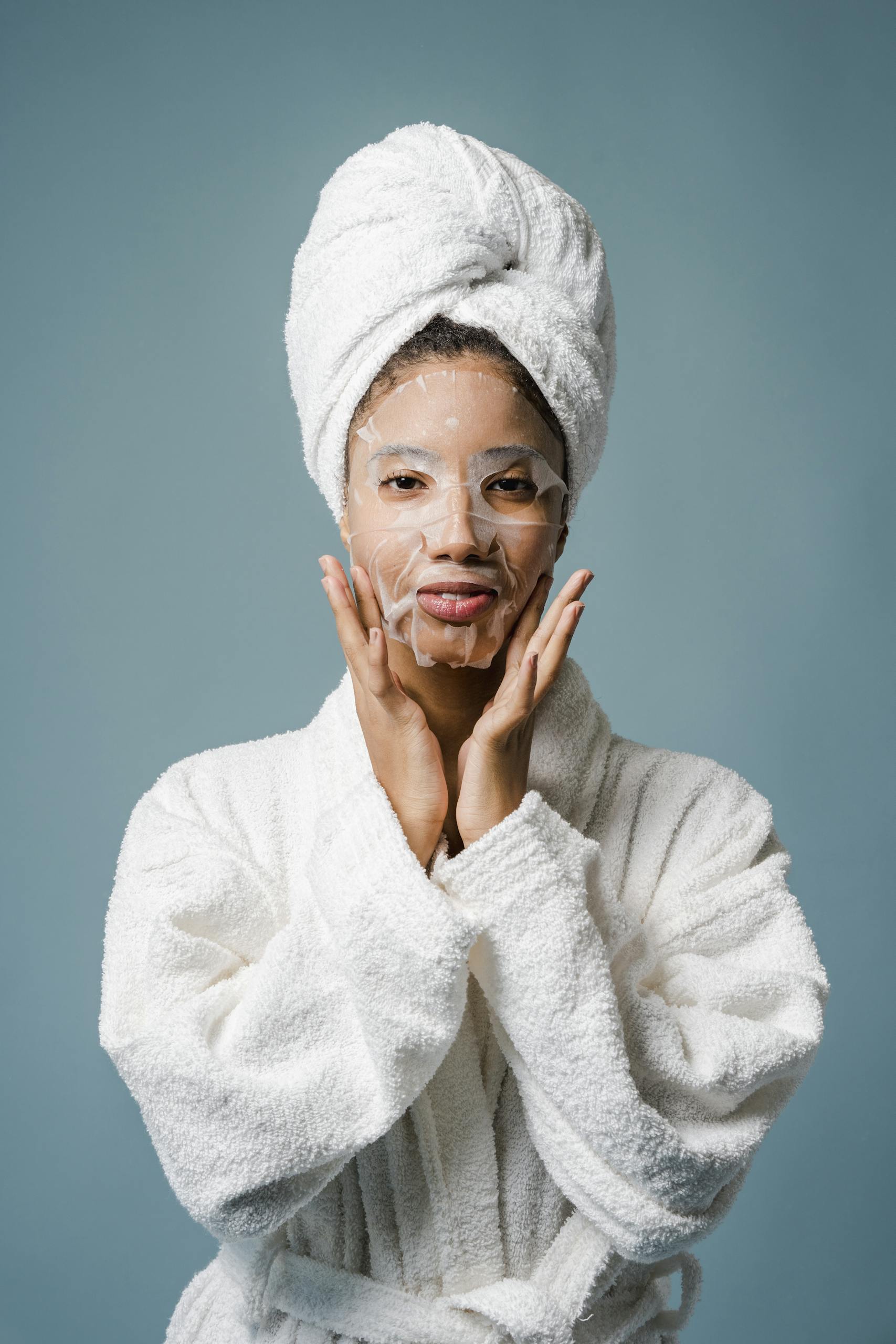 African American woman enjoying a home spa day with a sheet mask and towel wrap.