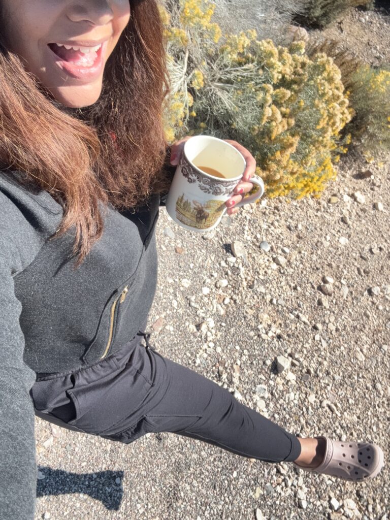 black woman wearing black joggers and crocs on a trail holding a cup of coffee