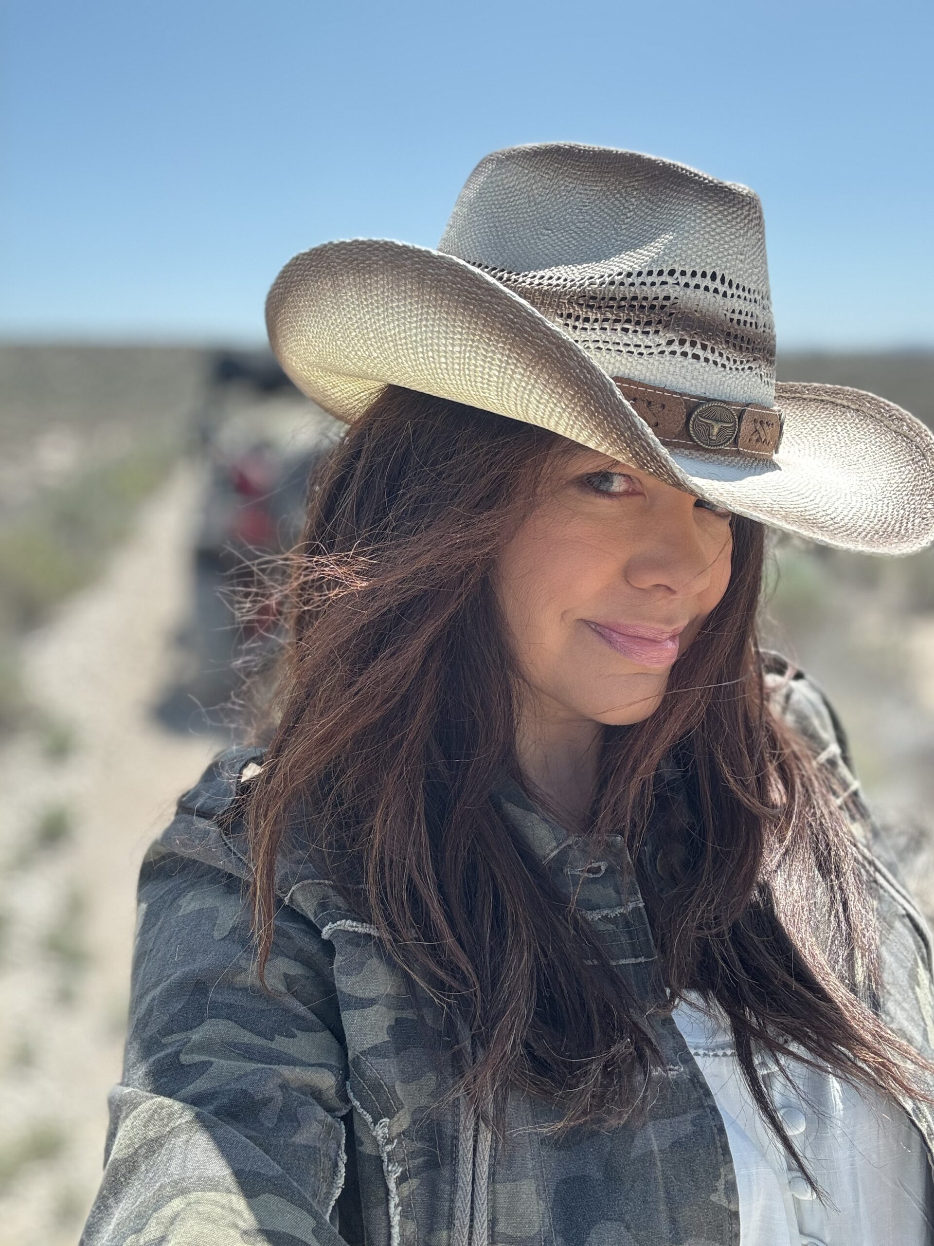 black woman wear a cowboy hat smining at the camera with an ATV in background with desert landscape