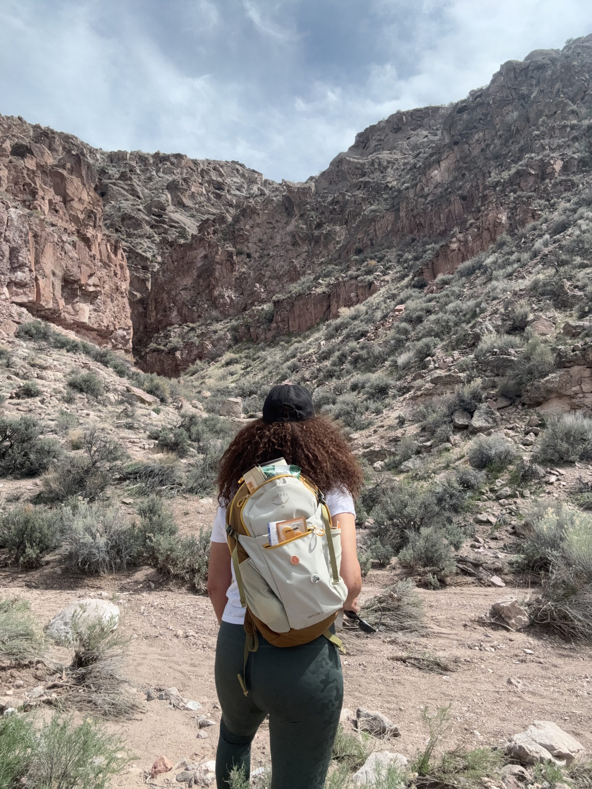 black woman with back turned to camera hiking in canyon wearing backpack