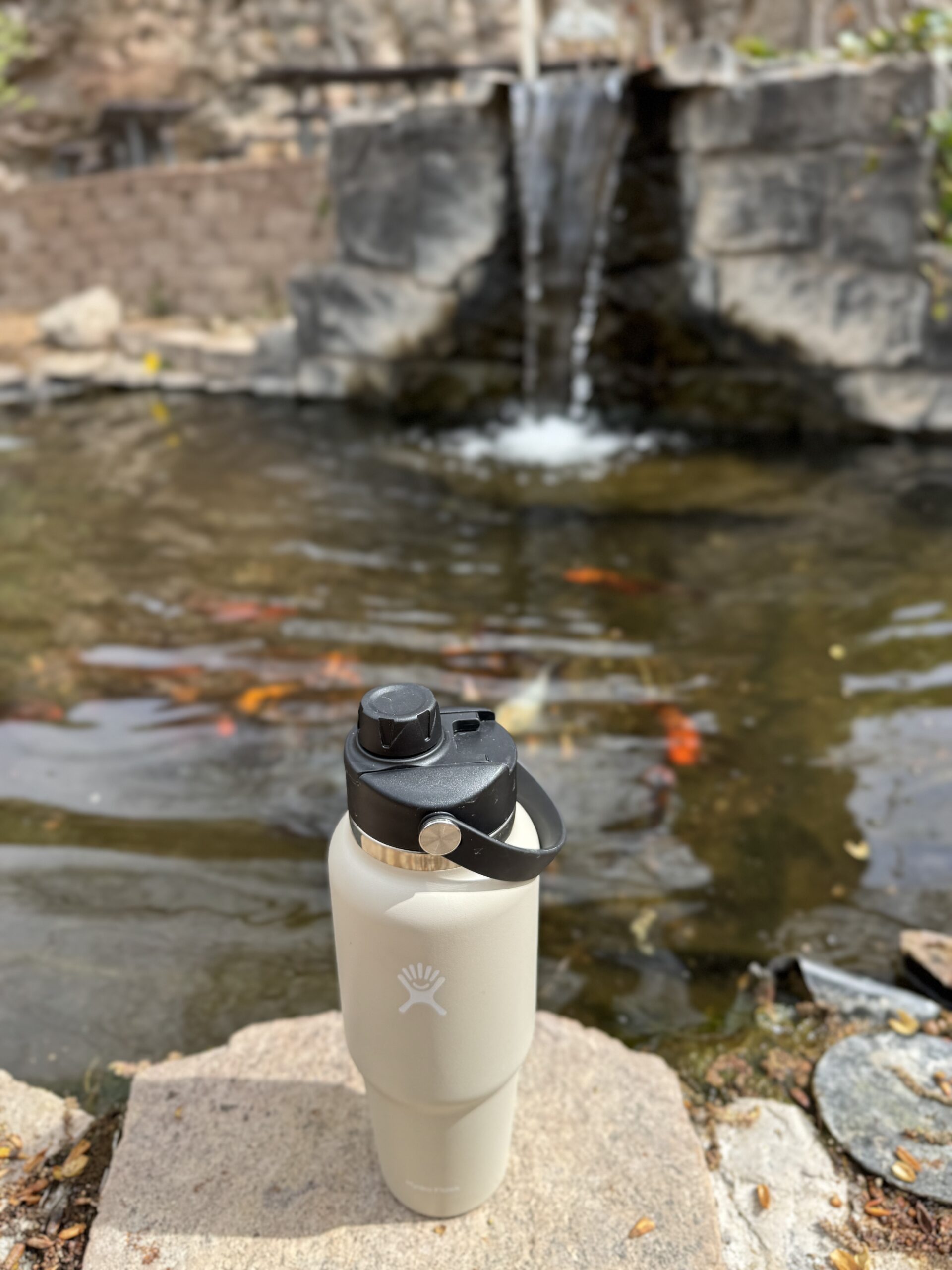 hydro flask water thermos on rock in front of waterfall and fish pond