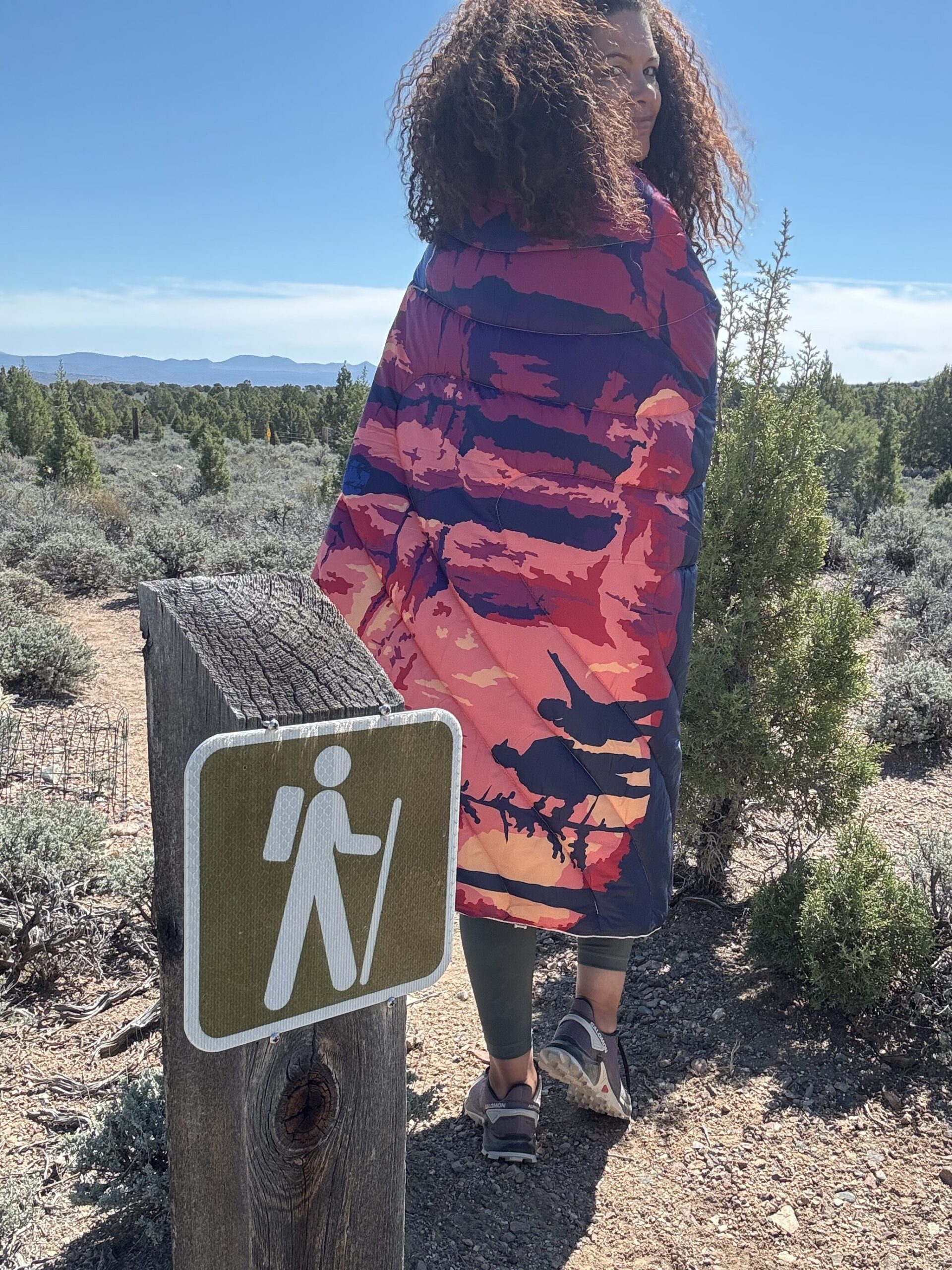 black women wrapped Rmpl outdoor colorful puffy blanket and sleeping bag on hiking trail i desert landscape