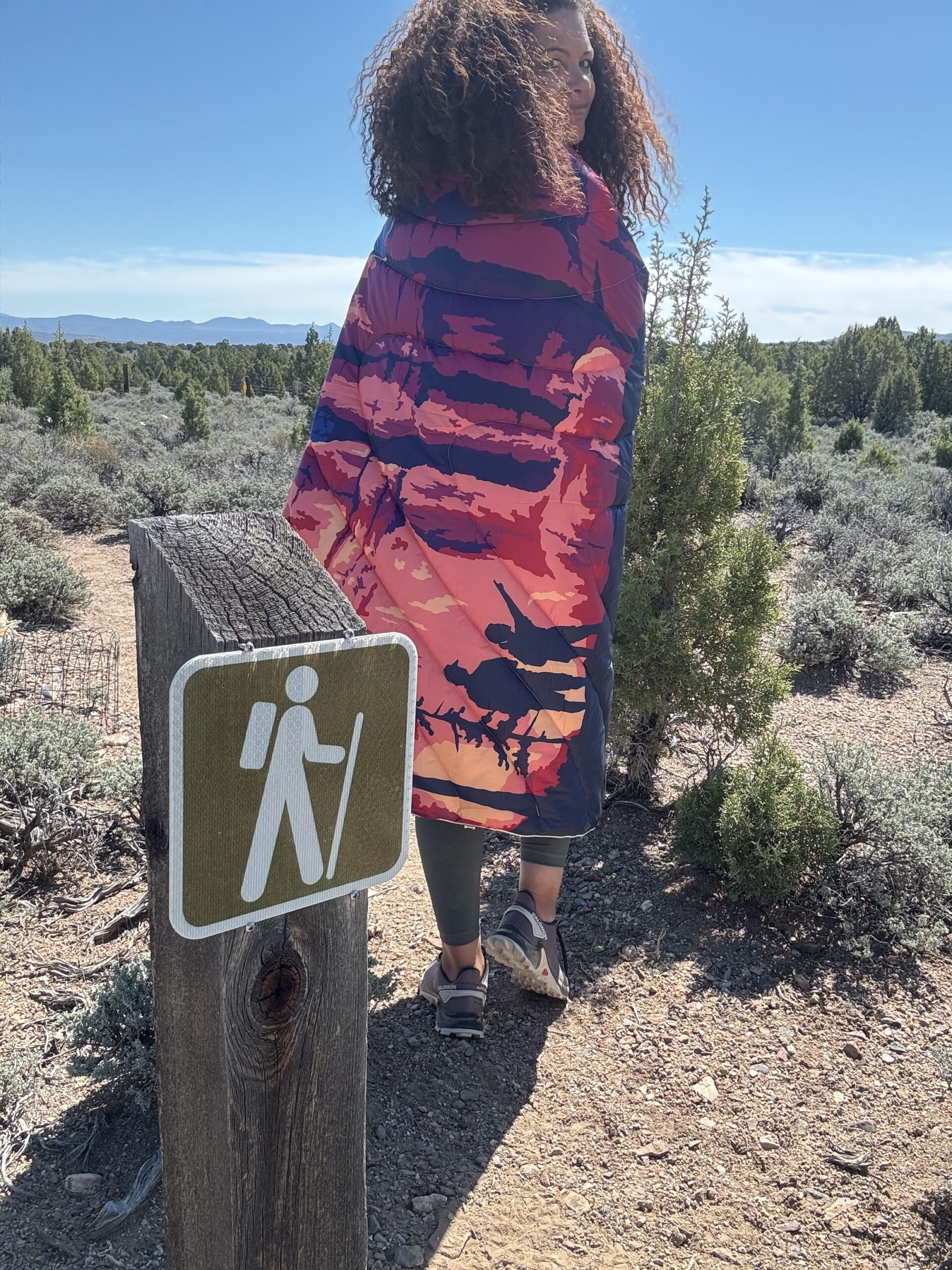 black women wrapped in colorful puffy blanket and sleeping bag on hiking trail