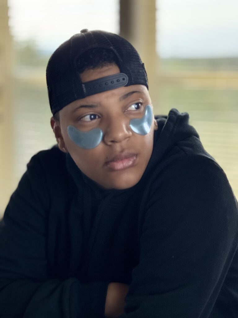 young black woman wearing eay patches and backwards hat looking right 