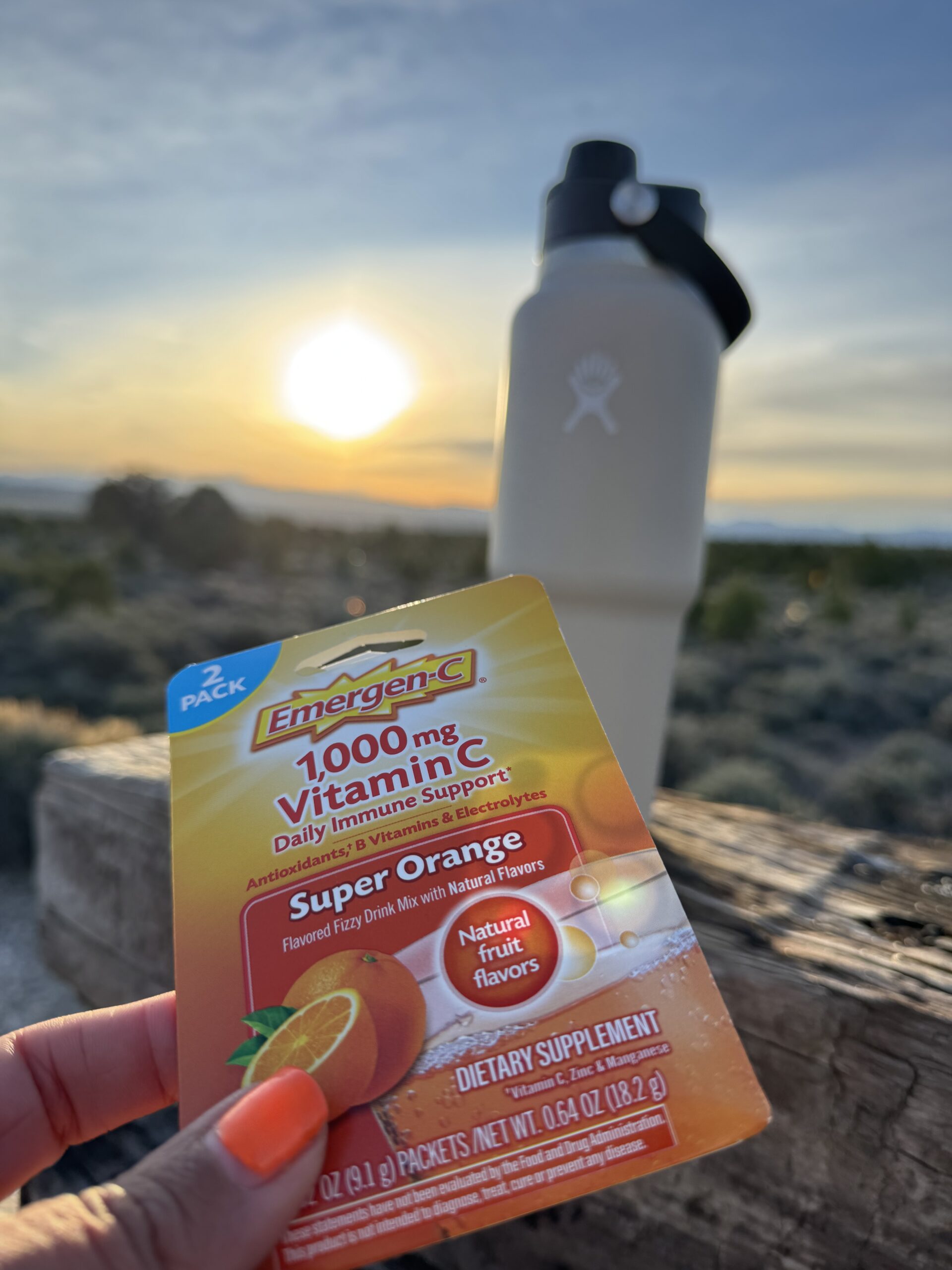 hand holding pack pf electolytes emergency packet in front of beige hydro flask watter bottle with sunrise in background