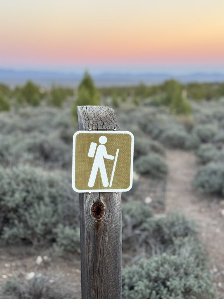hiking trail marker with a colorful sunset in the background of a desert landscape