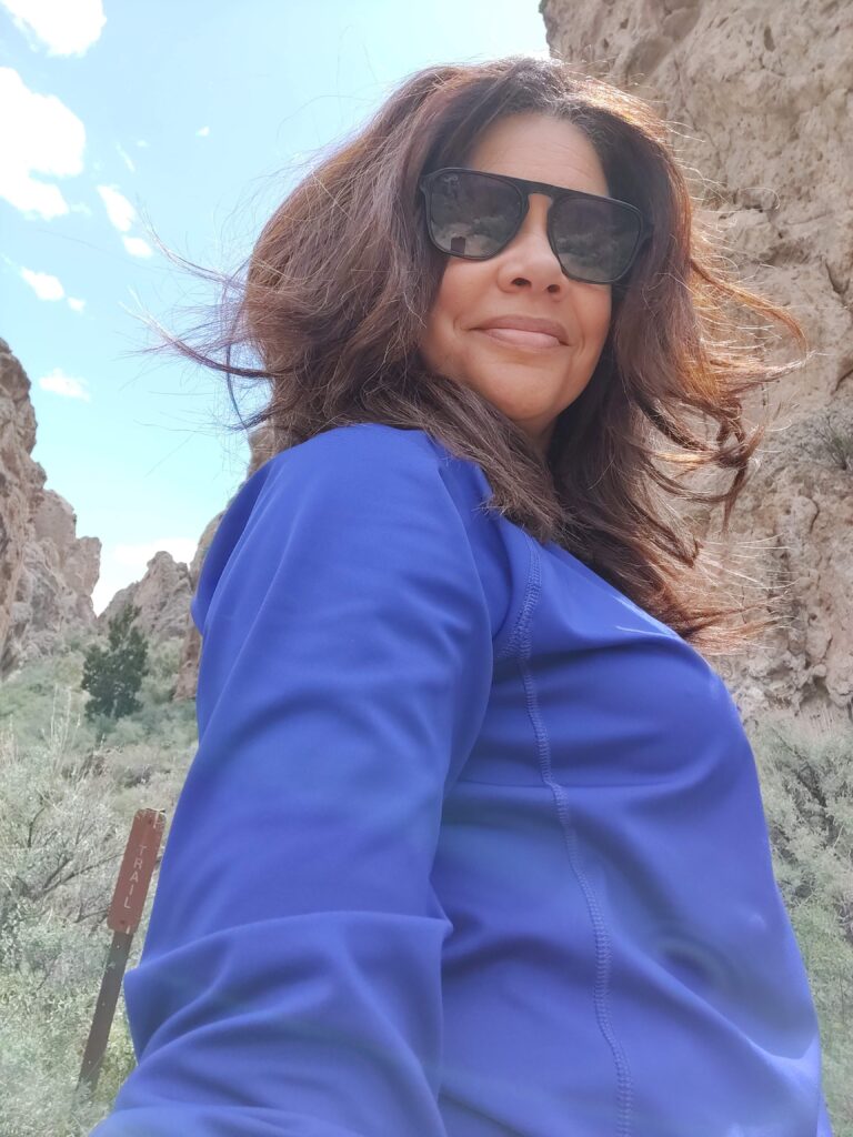 black woman in purple jacket and sunglasses on a hike in the desert landscape