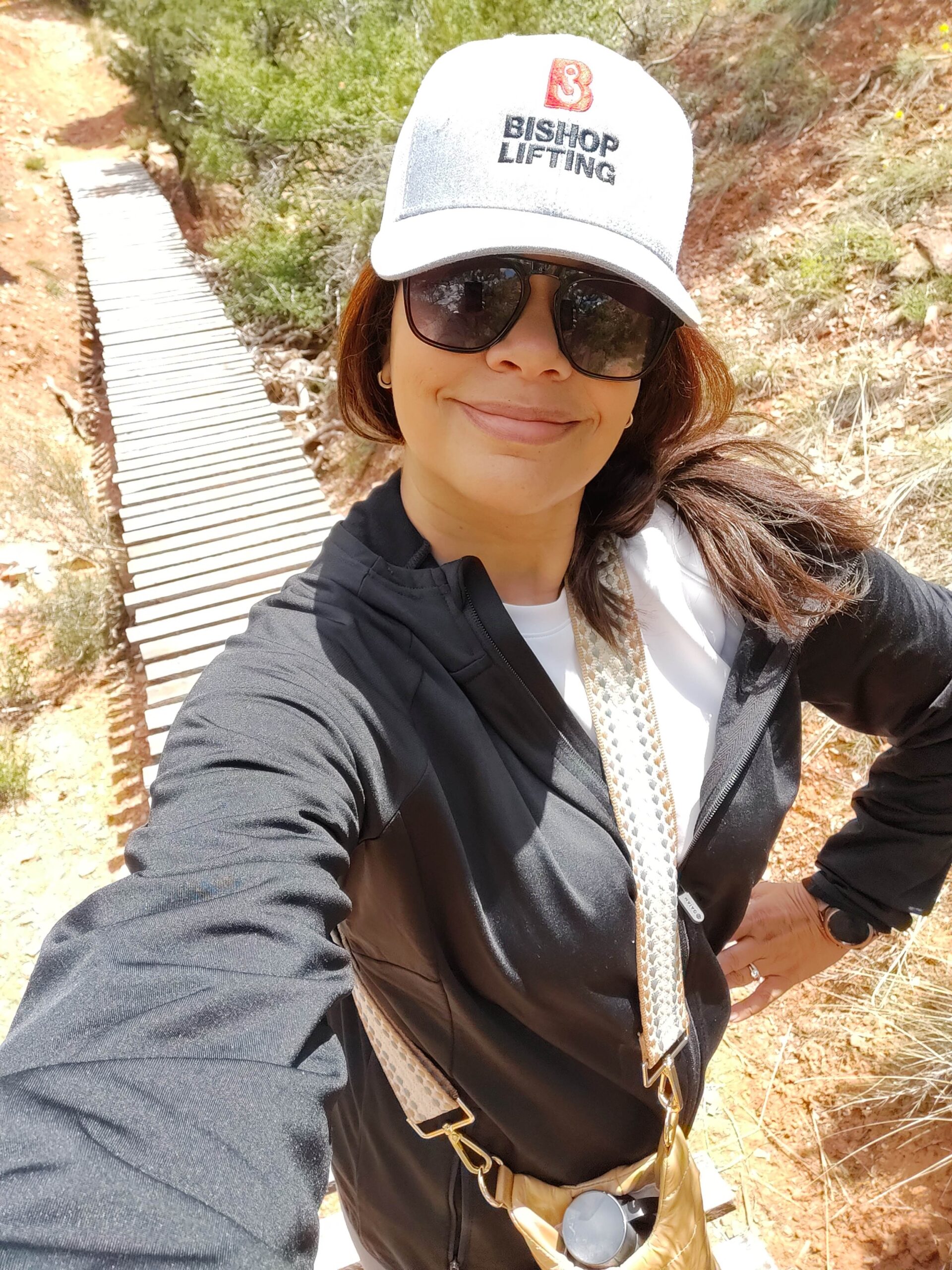 black woman wearing baseball hat and lightweight black zipup jacket on hike on a slatted bridge