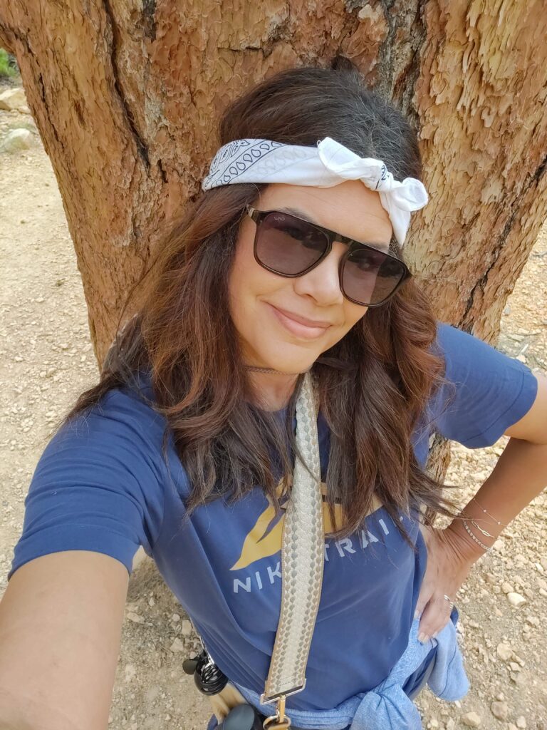 black woman wearing sunglasses and headband leading against tree trunk on hike in Bryce Canyon