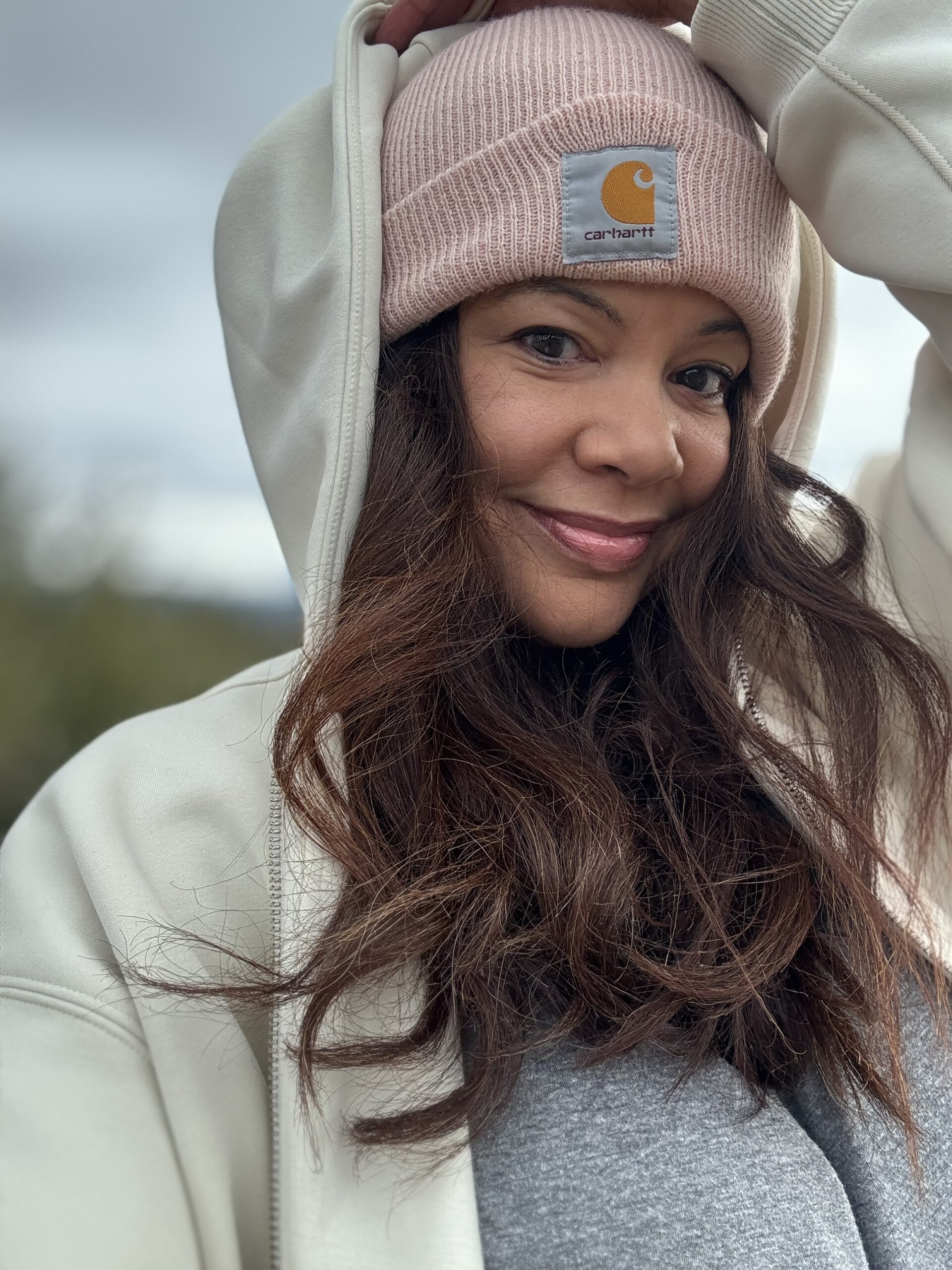 black woman in cream hoodie and carhart beanie smiling at the camera
