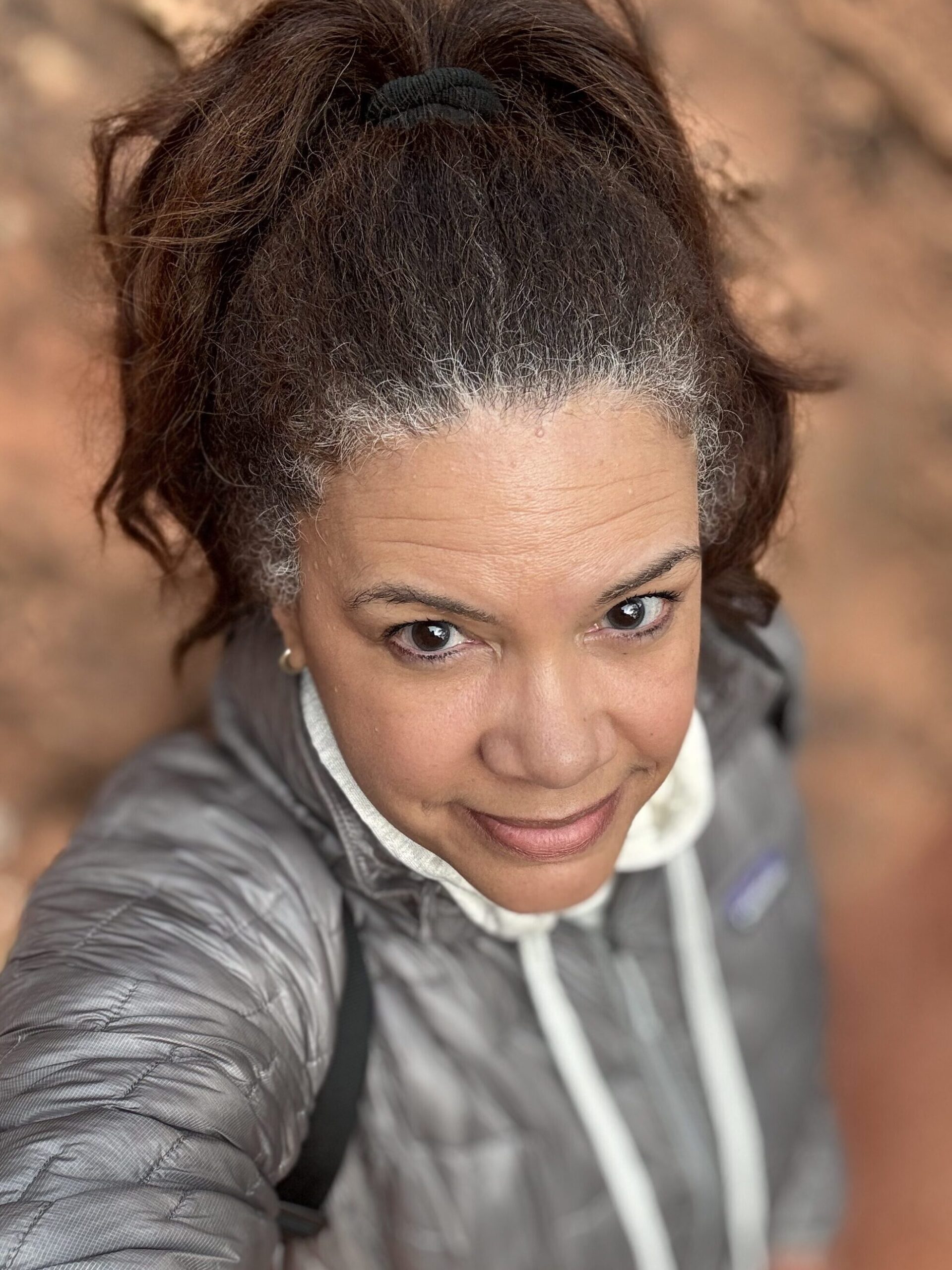 black woman wearing grey puffer patagonia jacket looking up at camera on hike in Zion National Park