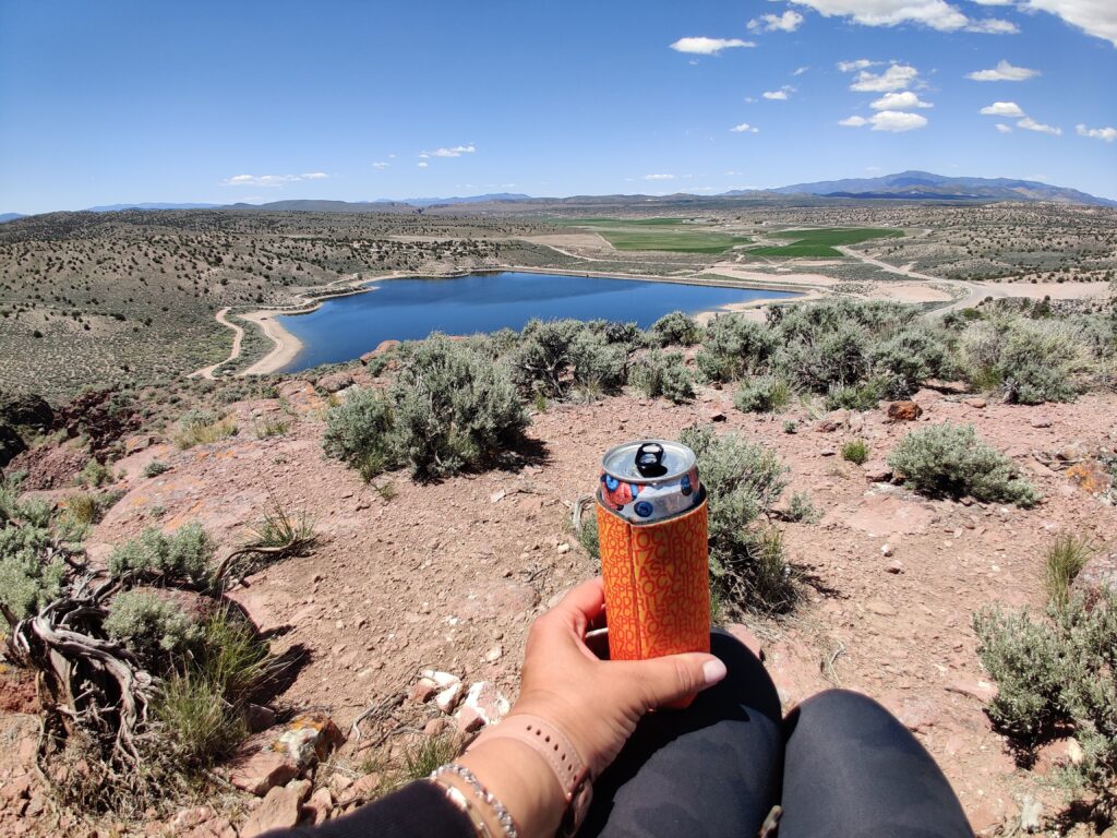 cold drink in a koozie while resting on a hike with lake in the background