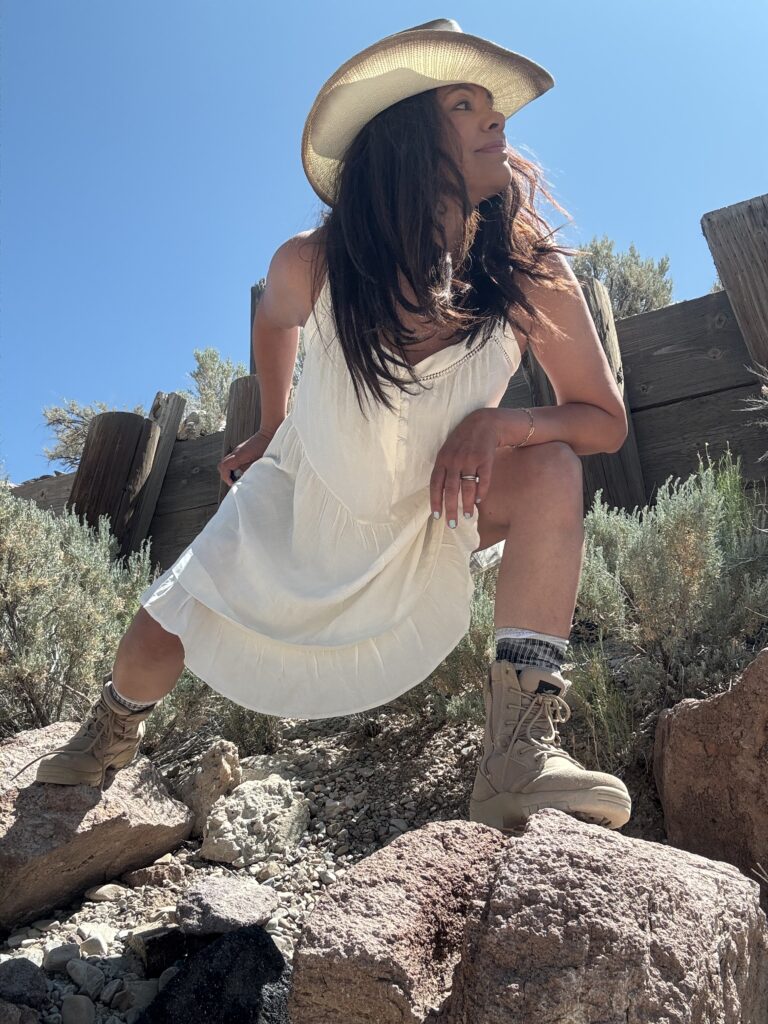 black woman in casual outfit in white dress and tan combat boots in a desert landscape