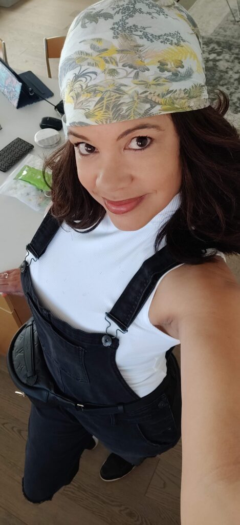 black woman looking at at camera wearing headband, white tank top and black overalls