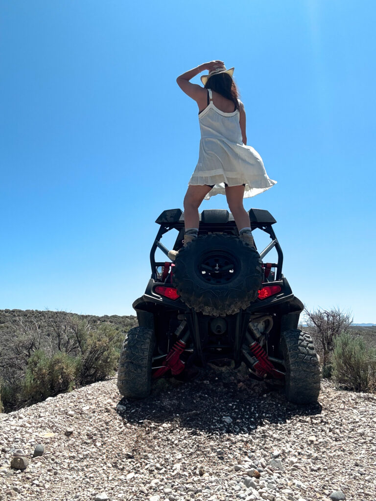 black woman standing on an ATV wearing white dress and construction or hiking hoots wearing cowboy hat