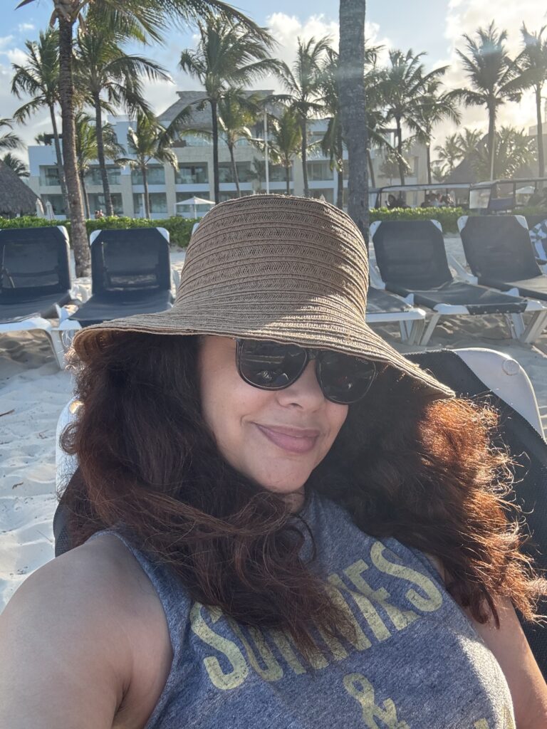 mixed race woman on vacation in dominican republic wearing hat and oversized sunglasses and drinking a beer on the beach